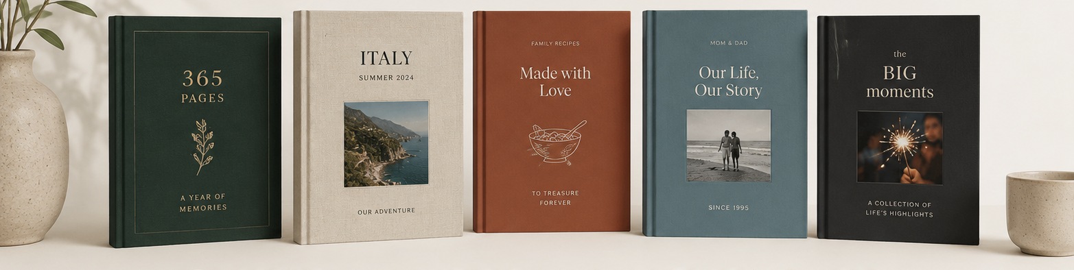 A row of five 365Pages journals (including yearly, Italy travel, family recipes, life story, and big moments editions) styled on a table with a plant and cup.